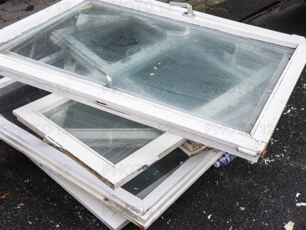 A pile of old white window frames with glass is lying on a sidewalk in Wuppertal, Germany