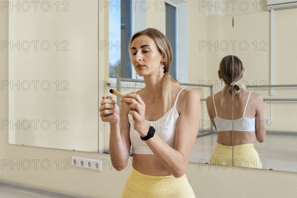 In a bright studio, a woman wearing a white top and yellow pants ignites palo santo the incense stick