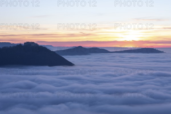 Sunset over the sea of fog from Beurener Fels to Hohenneuffen Castle, Swabian Alb, Baden-Württemberg, Germany. The Black Forest on the horizon