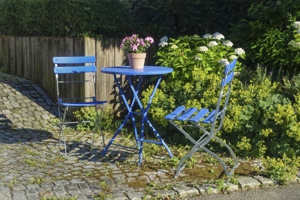 Blue garden chairs with small round table, idyll, petunias (petunia) in a plant pot, paving stones, plants, gardens, Germany