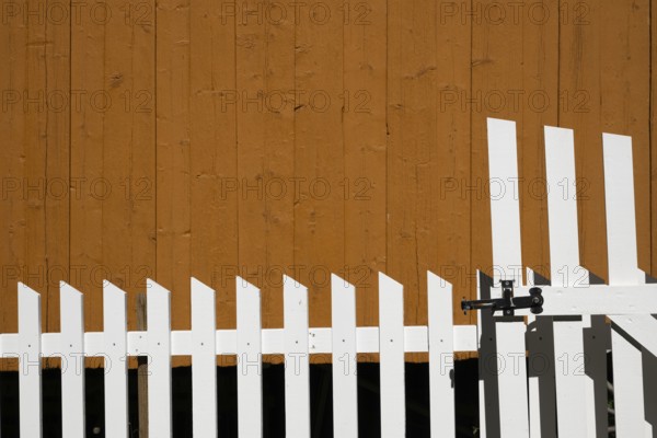 Yellow-painted wooden wall behind a white-painted fence, Maihaugen open-air museum with houses and objects from farms in Gudbrandsdal, Lillehammer am Mjøsa Lake, Innlandet Fylke Municipality, Norway