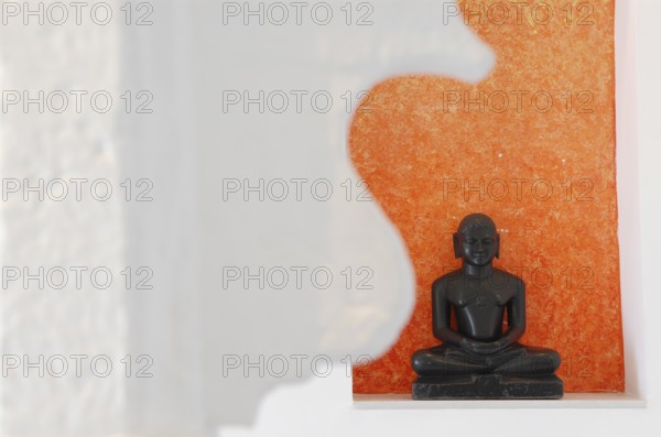 Statue of a black Buddha sitting meditating against an orange background, Devigarh Palace Hotel, near Udaipur, Rajasthan, India