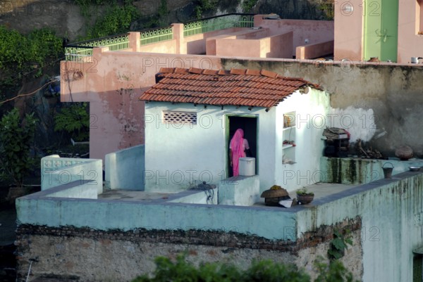 A woman wearing pink sari stands on the roof of a turquoise house, PDorf Delwara near Udaipur, Rajasthan, India