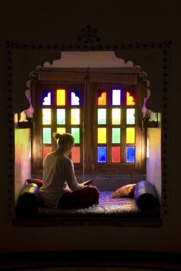 Woman sitting cross-legged reading in a room with colorful windows, calm and contemplative atmosphere, Palasthotel Karni Fort Bambora, Bambora, Rajasthan, India