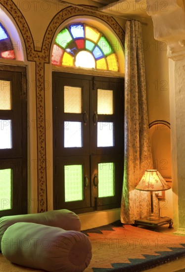 Interior with colorful window, cozy seating area with pillows and lamp, Karni Fort Bambora Palace Hotel, Bambora, Rajasthan, India