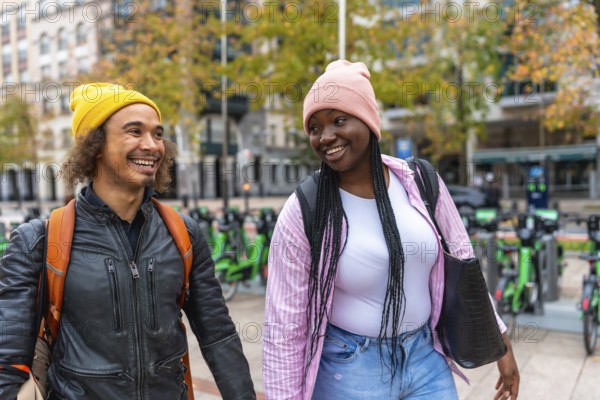 Diverse happy young adult friends are enjoying a cheerful walk together on a city street, smiling and engaging in conversation while exploring the urban environment
