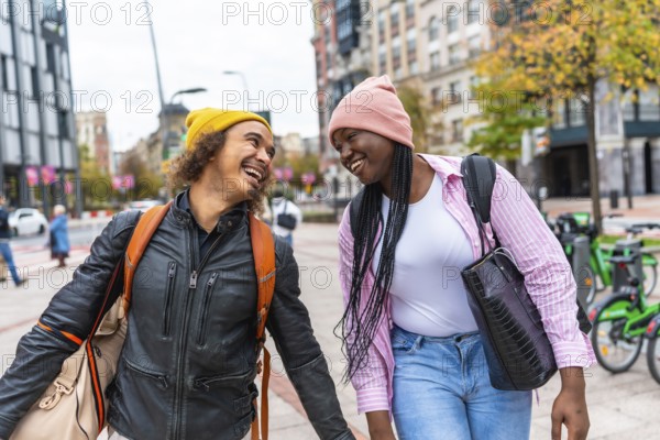 Happy young diverse couple walking together on a city street, sharing a joyful moment and laughing brightly while enjoying their time in an urban setting