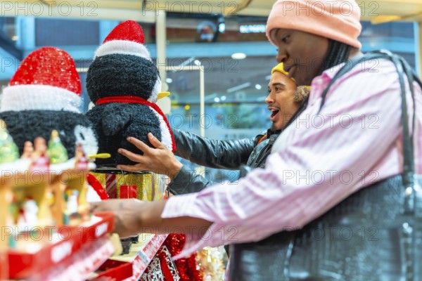 Diverse couple browsing holiday decorations in a store, a man looking surprised and excited while holding a penguin decoration, creating a joyful moment during christmas shopping