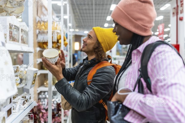 Young diverse couple browsing festive holiday decorations and gift ideas on department store shelves, smiling as they select seasonal presents and enjoy shopping together