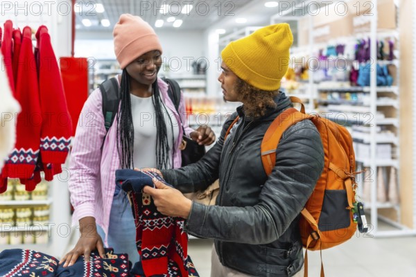 Young diverse couple choosing festive holiday ugly christmas sweaters in a retail store, enjoying winter fashion shopping and bonding during the holiday season