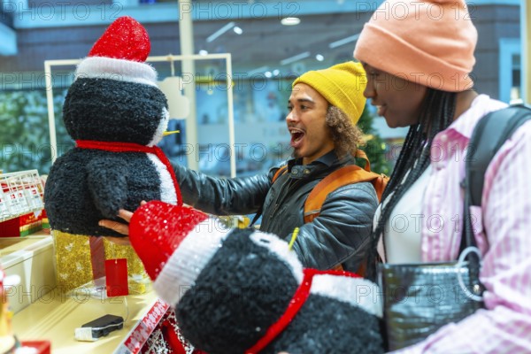 Young diverse couple excited discovering festive penguin decorations while shopping for holiday gifts and seasonal items, celebrating christmas spirit together in a retail store