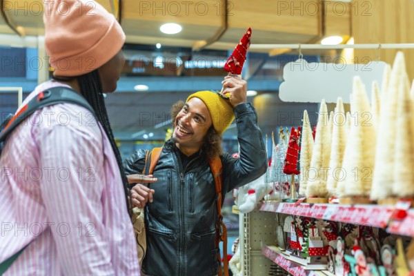 Diverse young couple laughing and shopping for festive holiday decorations in a bright store, enjoying playful togetherness and joyful winter season gift buying and merriment