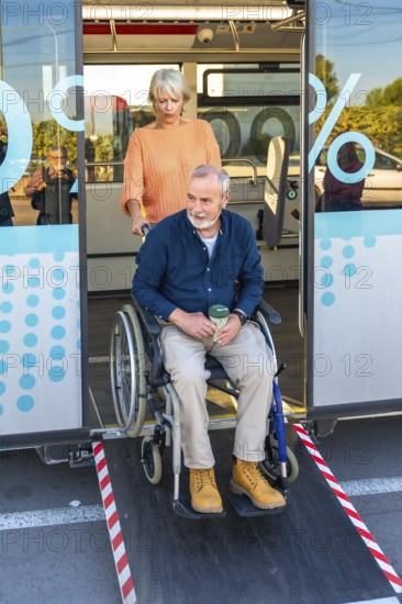 Senior woman is confidently assisting a mature man in a wheelchair to exit a public bus using the extended ramp, demonstrating care and accessibility in urban transportation