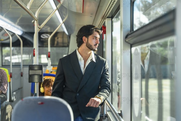 Young businessman in a suit jacket stands by a transit window, looking out pensively as the city moves by during his daytime commute on public transportation