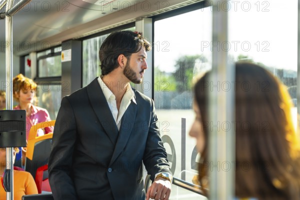 Young businessman in a dark suit stands on a city bus, gazing out the window as warm sunlight highlights his thoughtful expression during a downtown commute