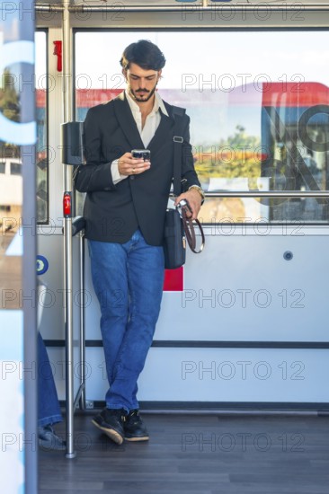Young man standing on a crowded bus, absorbed in his smartphone as he scrolls and messages during a daily commute, blending urban routine with digital connection