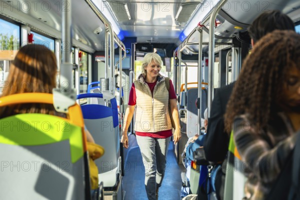 Senior woman smiling and walking along the aisle of a public bus, passengers traveling and sitting inside the urban vehicle, representing city life and modern transportation