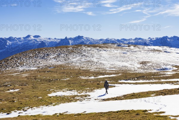 Female hiker walks across a snowfield on the Trattberg Alm with a view of the Tennengebirge, Osterhorn Group, Salzkammergut, Province of Salzburg, Austria