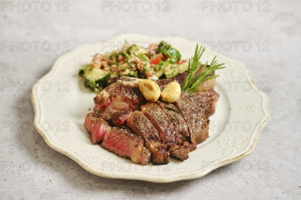 Juicy grilled steak on a vintage plate. Next to it, a vibrant tabbouleh salad features chopped tomatoes, cucumber and walnuts sprinkled with wine vinegar