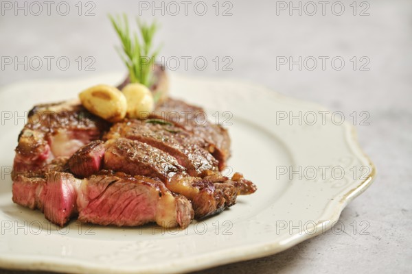 Juicy grilled cowboy steak on a decorative plate, enhanced with fresh herbs and garlic. This dish is perfect for a satisfying dinner, showcasing rich flavors and appealing presentation