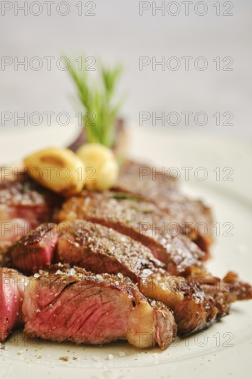 Close-up view of cowboy steak slices on a white plate. The meat is seared to perfection, showcasing a tender pink center. Fresh herbs and garlic add a flavorful touch to the dish