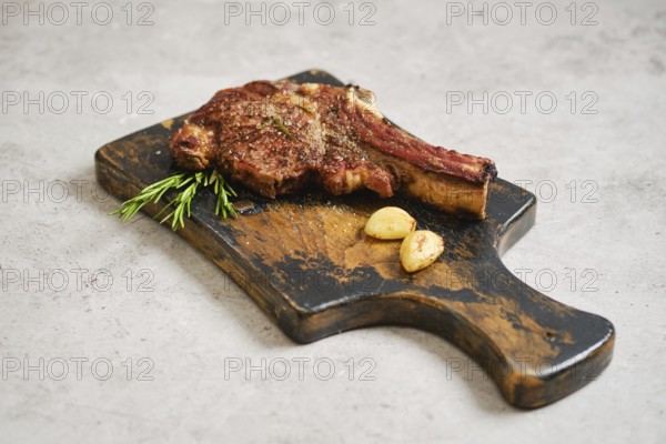 A juicy grilled cowboy steak on a rustic wooden cutting board. Garnished with fresh rosemary and roasted garlic cloves, this dish showcases a simple yet elegant meal perfect for any occasion