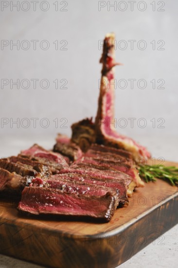 Thick slices of perfectly cooked t-bone steak medium rare on a wooden cutting board. Fresh herbs add a touch of green to the rustic scene