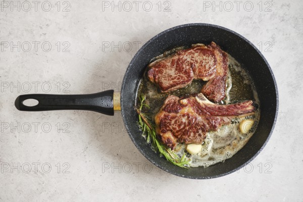 Two steaks - ribeye roll and cowboy sizzle in a skillet, surrounded by melted butter and fresh herbs. The scene showcases a simple cooking method that enhances the flavors of the meat