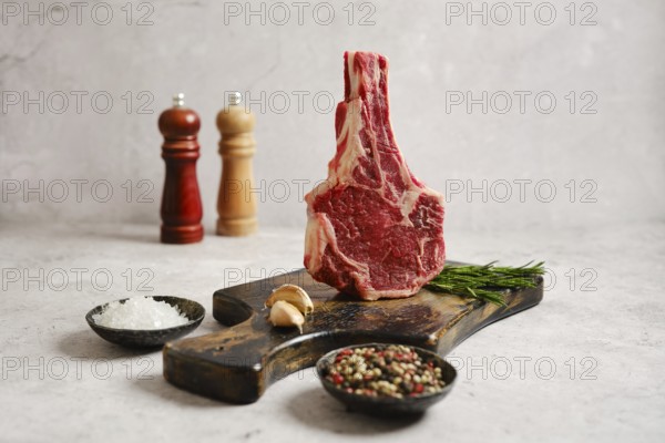 A raw cowboy steak on a wooden cutting board surrounded by fresh herbs. In the background, salt and pepper shakers add to the kitchen atmosphere, making it perfect for a gourmet meal preparation