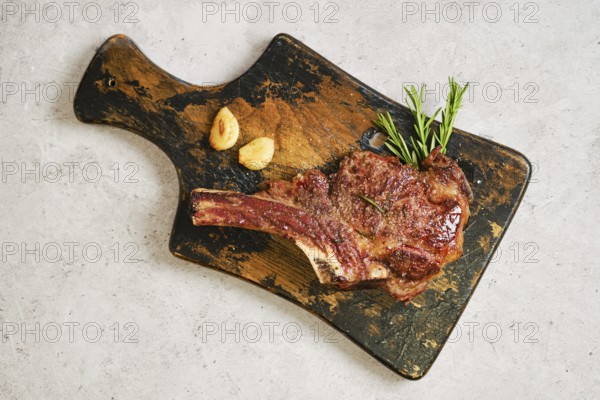 Grilled cowboy steak on a worn wooden cutting board, garnished with fresh rosemary and garlic. The rich brown color of the meat highlights its delicious sear, inviting a tasty dining experience
