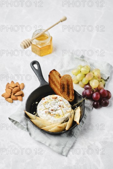 Soft brie cheese dish is baked in a small skillet, served with crispy bread, fresh pears, and crushed almonds. The scene captures a delightful mix of textures and flavors, perfect for sharing