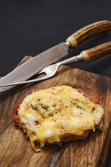 Tender pork chop topped with gooey melted cheese, served on a rustic wooden cutting board. Stainless steel knive and fork rest beside the dish, ready for serving