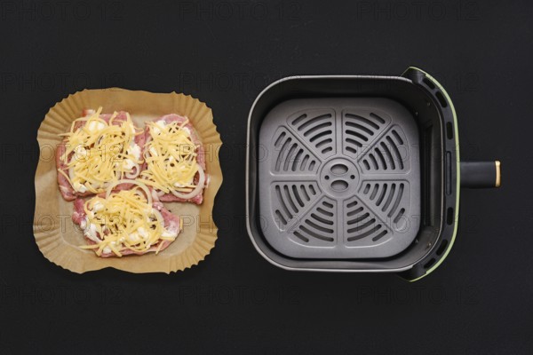 Three seasoned pork chops arranged on a parchment-lined tray, garnished with shredded cheese. Next to them, an air fryer basket sits empty, ready to cook the tasty meal