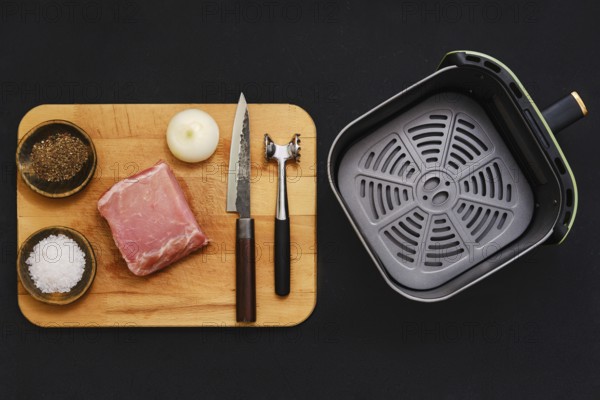 Raw pork tenderloin on a wooden cutting board alongside seasonings and kitchen tools. An onion, salt, and pepper are ready for flavoring before cooking in an air fryer