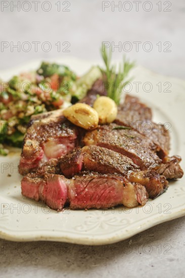 Juicy grilled steak rests on a decorative plate, served alongside a fresh salad made with vibrant greens, tomatoes, and grains. The dish is garnished with garlic for added flavor