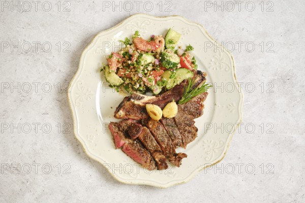 A delicious plate with perfectly grilled steak bone-in sliced into portions alongside a vibrant salad with tomatoes, cucumbers, and herbs. The meal looks inviting and nutritious for any occasion
