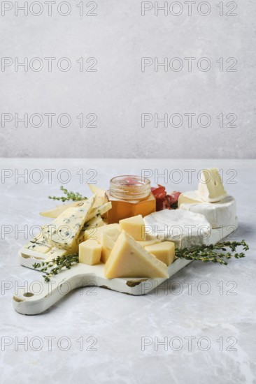 Fine selection of cheeses, honey, and herbs arranged artfully on a platter. Cubes of aged cheese, soft rounds, and honey jar create a tempting display, ideal for gatherings or casual snacking