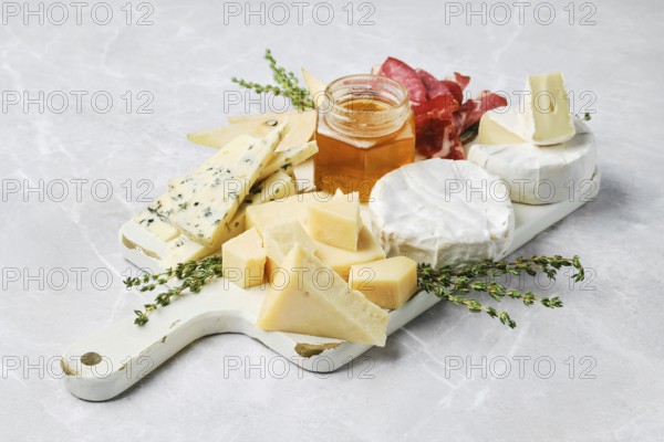 A beautiful spread featuring various types of cheese, honey in a jar, and slices of cured meat on a wooden board. Fresh herbs add a touch of color to the arrangement, making it visually appealing