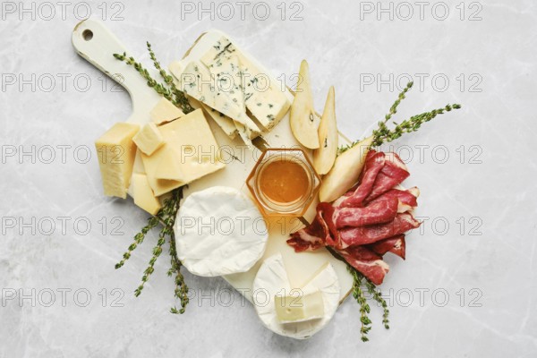 A beautifully arranged serving board features a variety of cheeses, cured meats, and fresh fruits. Honey in a small jar adds sweetness, while herbs enhance the presentation. Perfect for gatherings