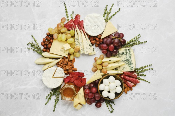 A colourful cheese and fruit platter displays a variety of cheeses, grapes, nuts, and cured meats, arranged in a circular shape, perfect for a social gathering or celebration