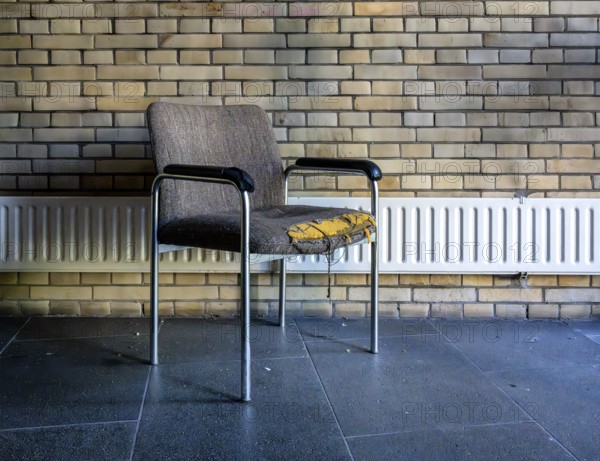 Retired and broken old office chair stands in front of a small radiator in an office building, Berlin, Germany