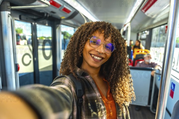 Young happy woman with curly hair wearing glasses and a plaid shirt, taking a selfie while traveling inside a public transport bus, showing a positive feeling on her daily commute