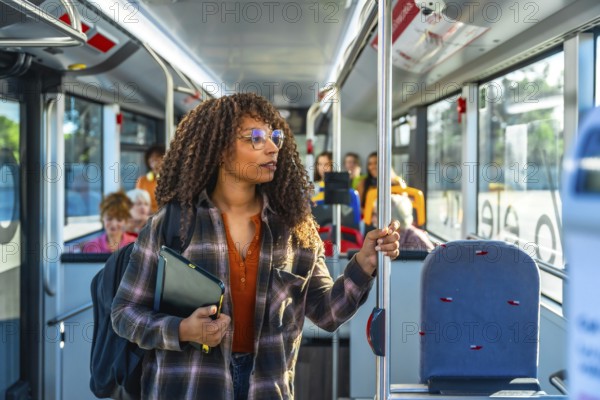 Young woman with curly hair and glasses stands inside a city bus holding a pole, wearing a backpack while commuting through urban streets during a daytime journey