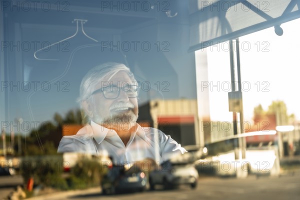 Senior bus driver smiling while looking outside through a window, reflecting street traffic, traveling and enjoying a journey, showing happiness and positive emotions during work