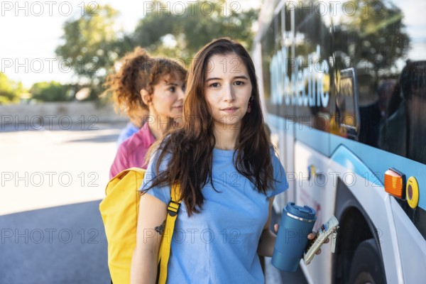 Young female commuters are standing in line, holding a reusable cup and a wallet, waiting to board a public bus, reflecting sustainable and urban transportation concepts