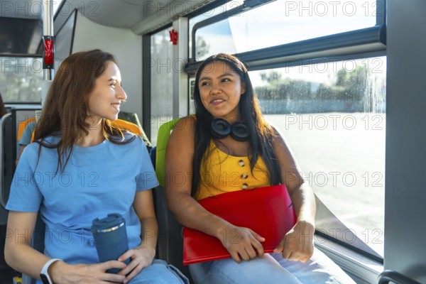 Two young diverse women students chatting and smiling on a city bus, enjoying a relaxed commute together between campus and urban life, sunlight through the window illuminating them