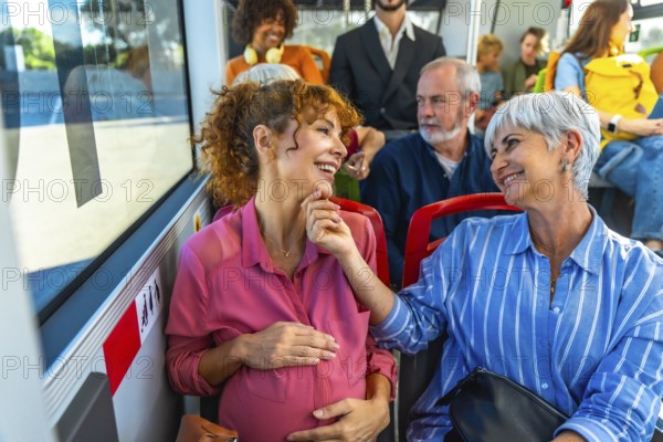Pregnant woman and senior woman are smiling and talking while traveling on a public bus, sharing a happy moment together in a diverse group of passengers