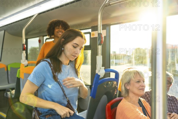 Diverse commuters on a city bus in sunlight, young woman looking down while other passengers sit and stand, candid urban transit scene showing daily travel and connection