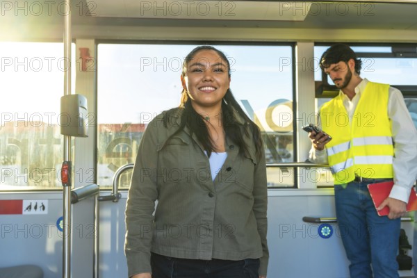 Smiling young woman standing inside a city bus during her daily commute, enjoying the ride while a fellow passenger checks his phone in the background, bright and casual atmosphere