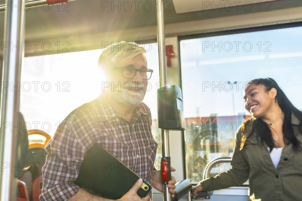 Two smiling passengers, an older man and a young woman, are traveling on a bus during daylight, experiencing a pleasant journey using public transportation